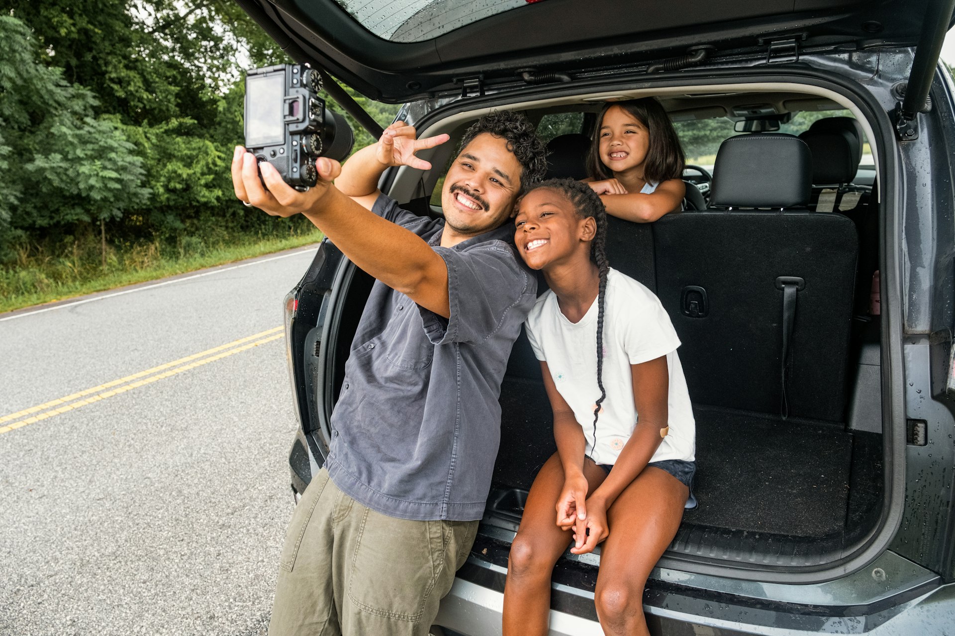 Father and daughters take a selfie by the car.